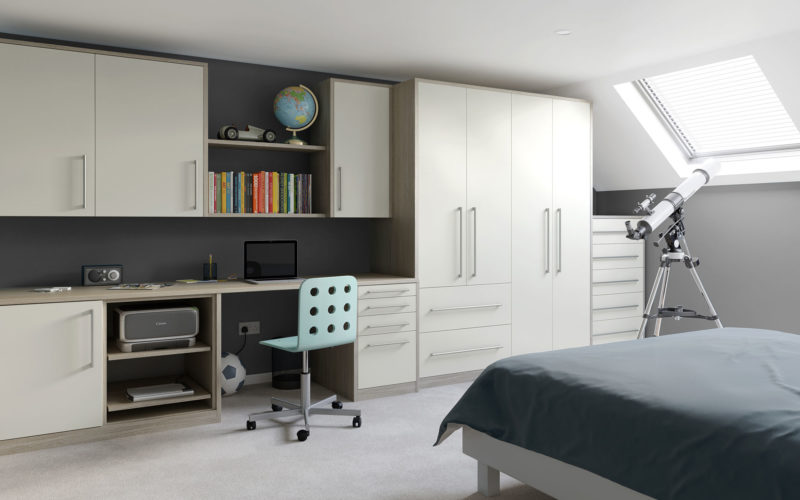 Modern attic bedroom with dark grey walls. Light coloured wood and white built in cupboard and desk unit. There is one long cupboard, one shorter cupboard with drawers underneath and the rest is cupboard spaces and drawers