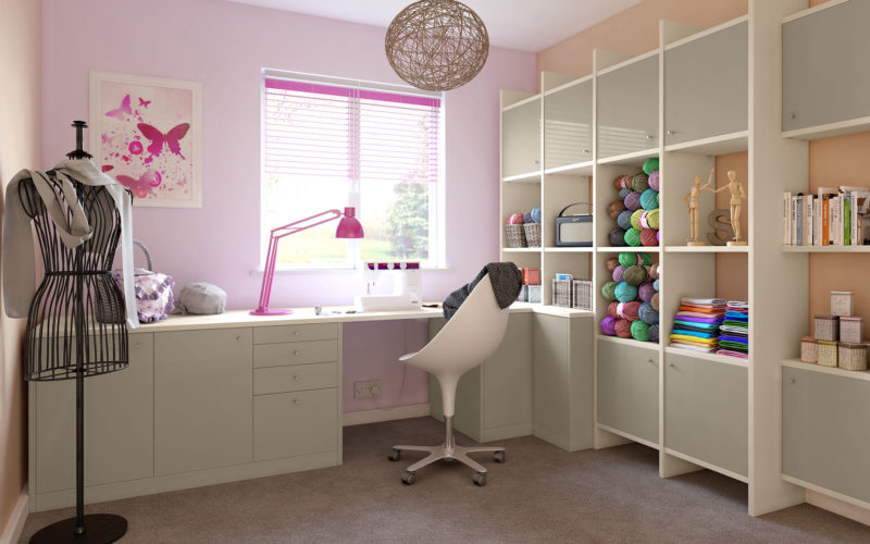 Pink craft room and office space. There is a desk which has cupboards built in. On the wall to the right there is a display unit which consists of storage space and display units