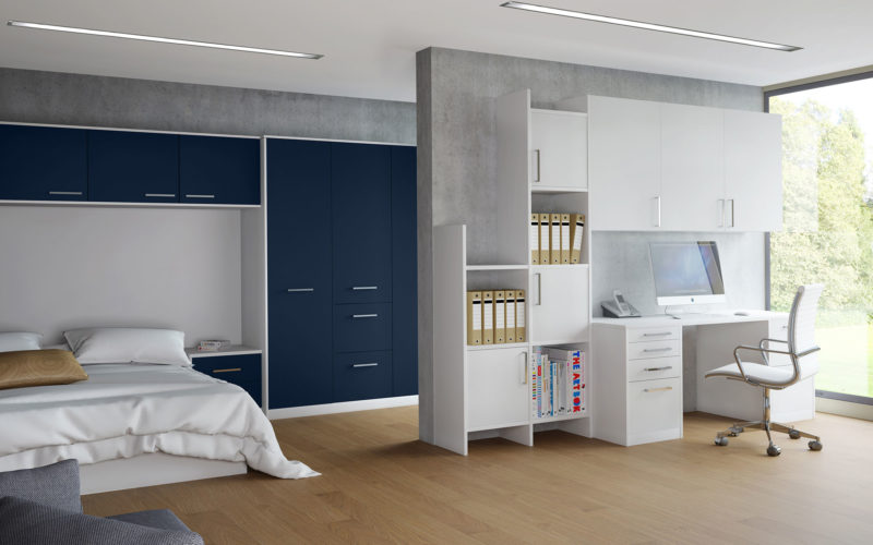 Modern light bedroom with cupboard surround which is in midnight blue. There is also a desk unit which compromises of a desk and a display and cupboard unit.