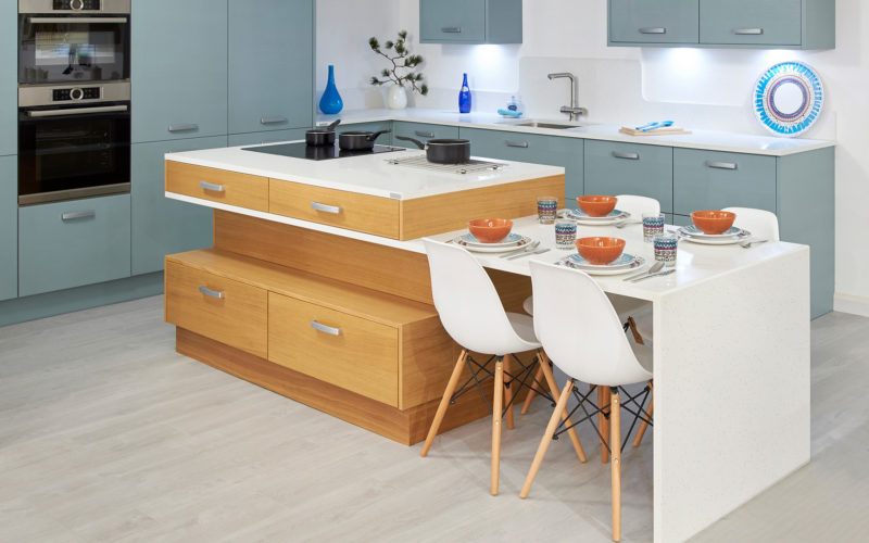 Aqua coloured cabinets with white counter tops. A orange wood kitchen island with white counter top that extends to a white table with four seats.