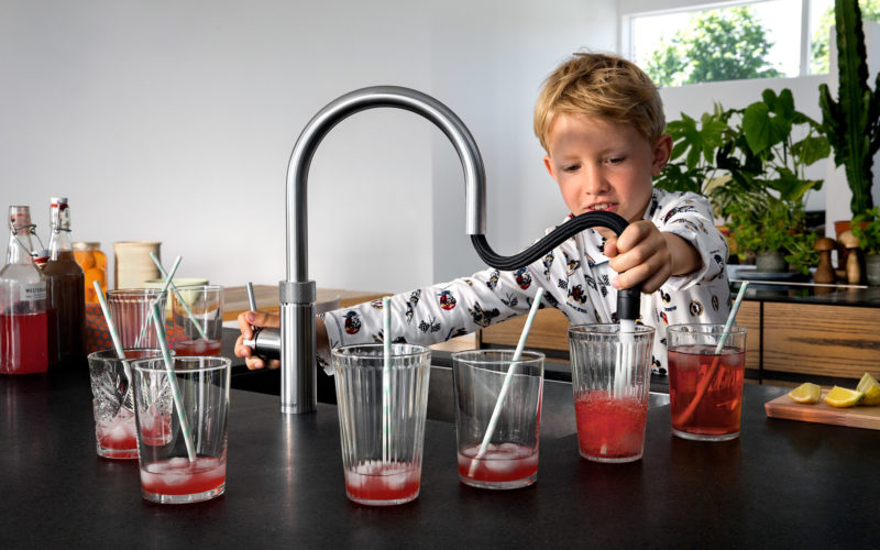 Quooker hot tap showing extendable tap with little boy using it to make multiple glasses of squash