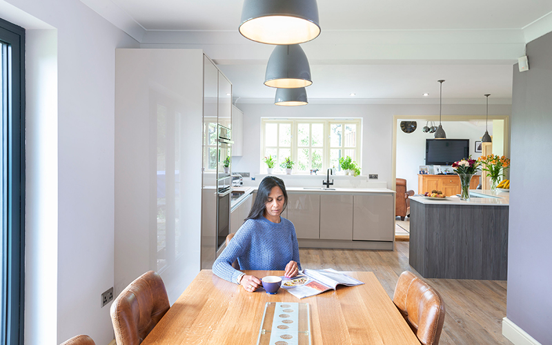 Woman sitting at dining table in neutral handeless kitchen installed by the KBB Centre