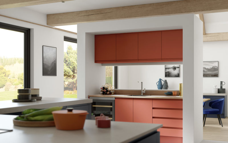 Terracotta coloured kitchen cabinets on one side of the room, showcasing the amazing colour. Along with the other cupboards being grey, all with a creamy white coloured top. Integrated drinks fridge on the side of the terracotta cabinets.