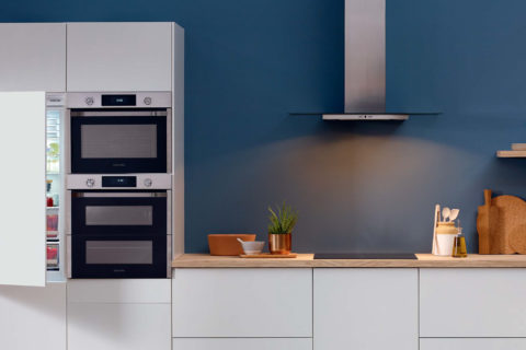 Samsung hob with extractor fan and ovens in a modern kitchen which is light grey cabinets and wooden counter tops