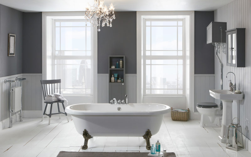 An airy bathroom showroom in Ipswich that features a large white bathtub in the middle on silver legs, with grey and white walls and large windows
